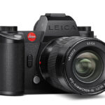 Black Leica mirrorless camera with lens on a white background.